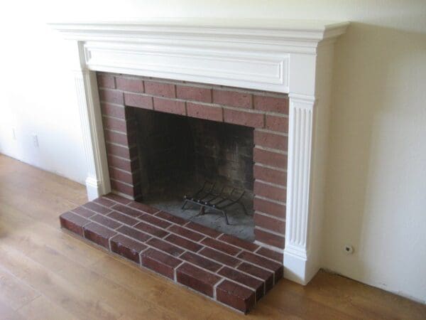 A fireplace with brick and white trim in the corner.