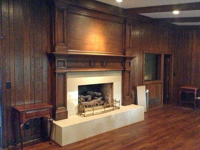 A fireplace in the center of a room with wood paneled walls.