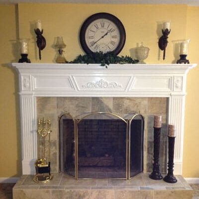 A fireplace with a clock above it and candles on the mantle.